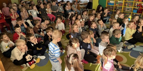 przedszkolaki siedzące na dywanie, ilustrujące ruchem treść wierszyka